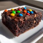 Close-up of a rich, fudgy cosmic brownie topped with chocolate frosting and colorful candy pieces.