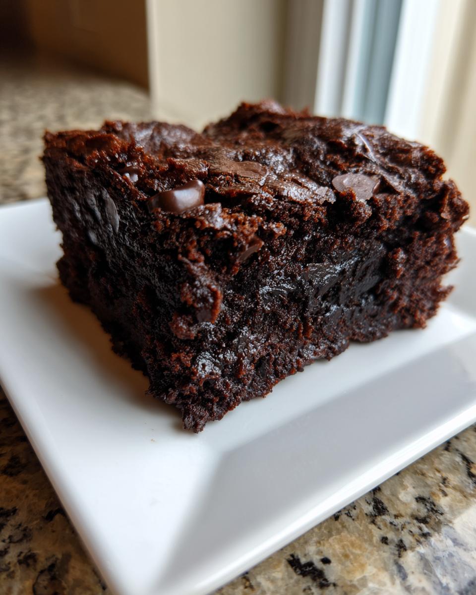 Close-up of a rich, fudgy slice of zucchini brownies topped with melted chocolate chips on a white plate.