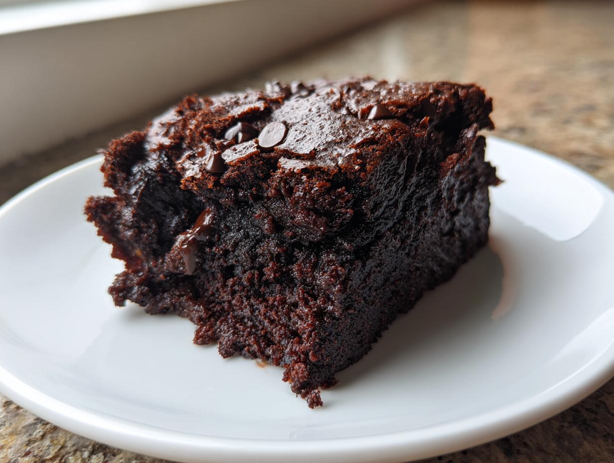Close-up of a rich, dark, fudgy slice of zucchini brownies topped with melted chocolate chips on a white plate.