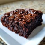 A close-up of a rich, fudgy zucchini brownie square topped with melted chocolate chips.