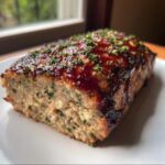 A thick slice of moist garlic parmesan chicken meatloaf topped with a dark, glossy glaze and fresh parsley.