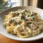 Close-up of creamy garlic parmesan chicken pasta with fettuccine, topped with chicken chunks, grated cheese, and parsley.