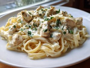 Close-up of creamy garlic parmesan chicken pasta with fettuccine noodles, topped with chicken chunks and fresh parsley.
