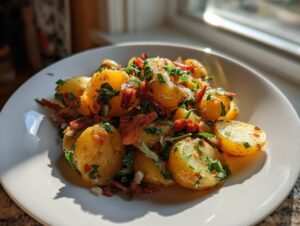 A white plate filled with warm German potato salad featuring golden potatoes, crispy bacon bits, and fresh parsley.