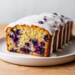 Close-up of a freshly baked blueberry zucchini bread loaf topped with white glaze, showing moist crumb and blueberries.