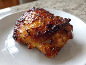 Close-up of a perfectly cooked, glazed, and caramelized chicken thighs piece on a white plate.
