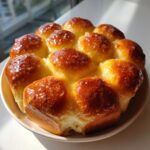 A cluster of golden brown, shiny dinner rolls baked together in a pan, glistening with a glaze.