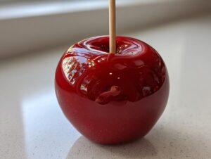 Close-up of a single, perfectly coated, glossy red candy apple resting on a light countertop.