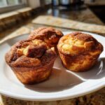 Three golden gluten free cinnamon sugar french toast muffins dusted heavily with cinnamon sugar on a white plate.
