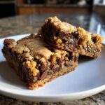 Two thick, gooey chocolate chip cookie bars stacked on a white plate, showing melted chocolate chips.