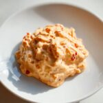 A dollop of creamy, orange-hued healthy big mac sauce speckled with visible red pepper flakes, served on a white plate.