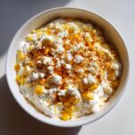 Overhead view of a creamy high protein elote dip topped with crumbled white cheese and chili powder.