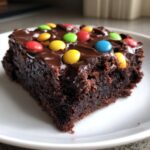 Close-up of a fudgy square of homemade cosmic brownies topped with chocolate frosting and colorful candy pieces.