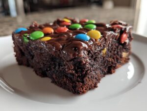 Close-up of a rich, fudgy slice of homemade cosmic brownies topped with chocolate frosting and colorful candy pieces.