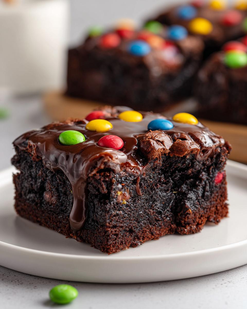 A close-up of a rich, fudgy homemade cosmic brownies square topped with melted chocolate glaze and colorful candy-coated chocolates.