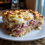 A thick slice of homemade Reuben bake featuring layers of corned beef, sauerkraut, and melted Swiss cheese.