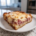 A square slice of homemade Reuben bake with corned beef, sauerkraut, and melted Swiss cheese on rye bread.