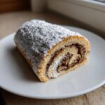 A cross-section slice of italian nut roll cookies filled with nuts and powdered sugar on a white plate.