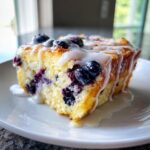 A close-up slice of lemon blueberry french toast casserole topped with a thick vanilla glaze and fresh blueberries.
