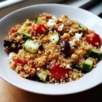 Close-up of a vibrant quinoa salad featuring chickpeas, cucumber, tomatoes, olives, and feta cheese.
