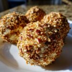 Close-up of four individual mini cheese ball appetizers coated generously in chopped nuts.