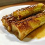 Close-up of three pieces of perfectly caramelized miso braised leeks glistening with glaze on a white plate.