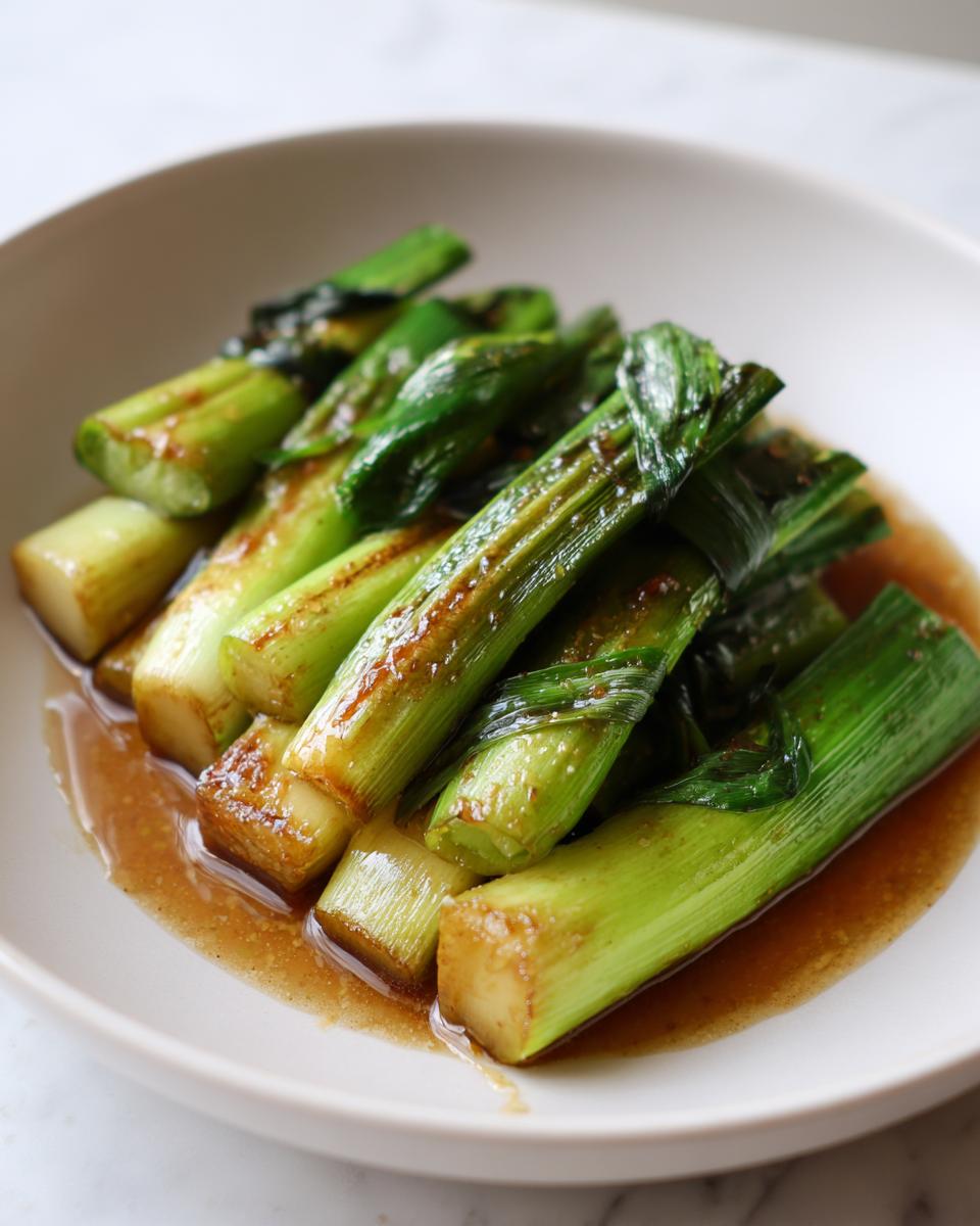 Close-up of tender miso braised leeks served in a light brown, savory sauce in a white bowl.