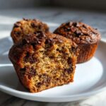 Close-up of a moist banana muffins cut in half showing chocolate chips inside and on top.