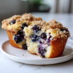 Close-up of moist blueberry muffins cut in half, showing juicy blueberries and crumb topping.