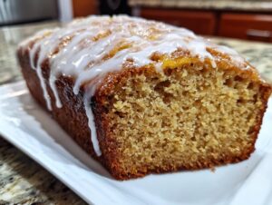 Close-up of a slice of moist eggnog bread showing the crumb texture, topped with a thick vanilla glaze drizzle.