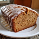 Close-up of a freshly baked, moist eggnog bread loaf drizzled generously with white vanilla glaze.