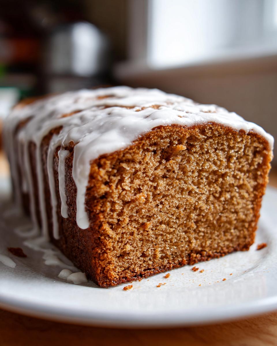 Close-up of a moist eggnog bread loaf with thick white glaze drizzled across the top, sitting on a white plate.