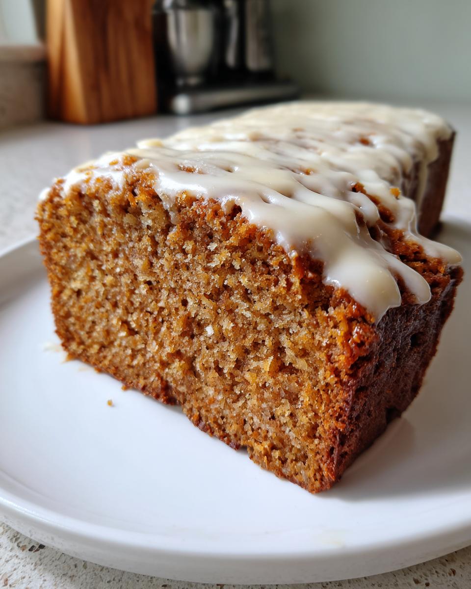 Close-up of a moist slice of eggnog bread topped with a thick white glaze, resting on a white plate.