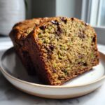 Close-up of two slices of moist zucchini bread packed with shredded zucchini and chocolate chips, served on a small plate.