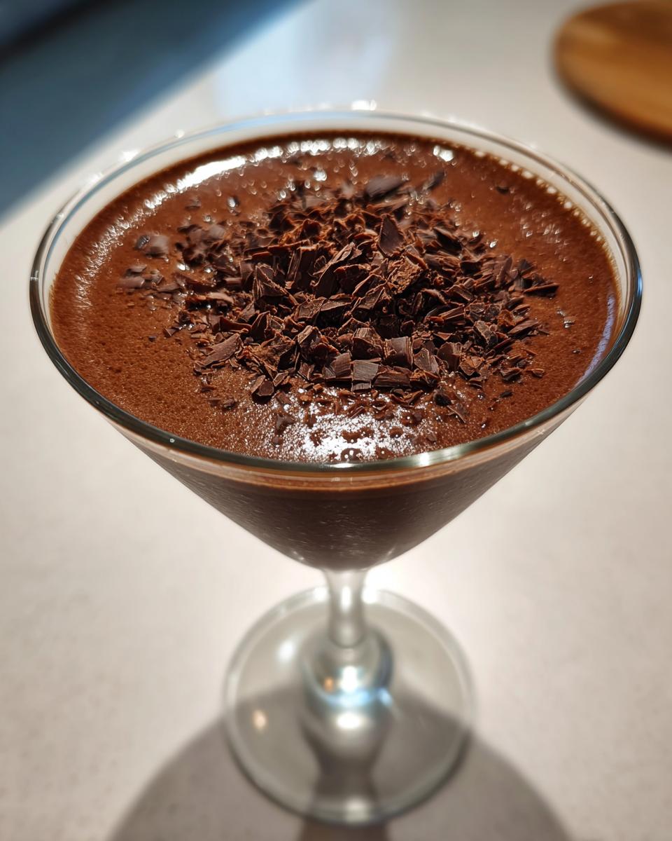 A close-up of a rich, dark brown non alcoholic chocolate martini topped with chocolate shavings in a stemmed glass.