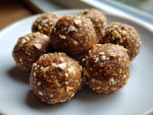 A pile of delicious peanut butter protein balls coated in chopped nuts on a light gray plate.