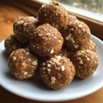 A stack of homemade peanut butter protein balls coated in chopped peanuts on a white plate.
