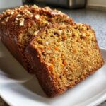Two thick slices of moist persimmon bread, topped with walnuts, displayed on a white plate.