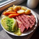 A white plate featuring sliced slow cooker corned beef and cabbage, carrots, and potatoes.