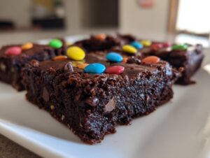 Close-up of fudgy protein cosmic brownies topped with colorful candy-coated chocolates on a white plate.