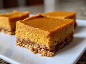 A close-up of a square pumpkin cheesecake bars slice showing the thick, orange filling and crumbly graham cracker crust.
