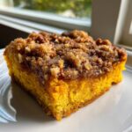 A close-up of a moist slice of pumpkin dump cake with a thick, crunchy pecan streusel topping.