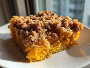 Close-up of a moist slice of pumpkin dump cake featuring a rich orange filling and a thick, crumbly brown sugar streusel topping.