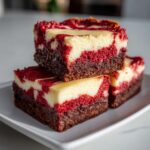 Three stacked squares of rich red velvet cheesecake brownies featuring dark chocolate base and cream cheese swirl.