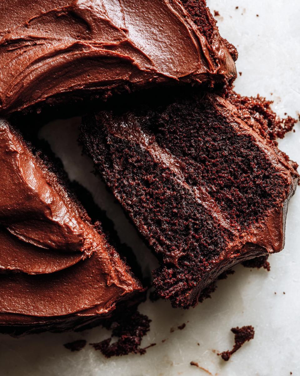 Close-up of a rich, dark chocolate cake slice being pulled away, covered in thick chocolate ganache frosting.