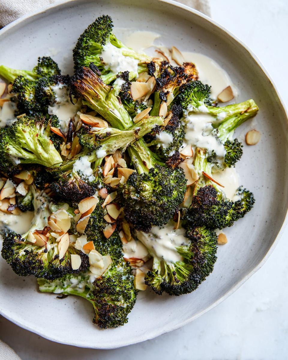 Close-up of perfectly roasted broccoli salad florets drizzled with creamy dressing and topped with sliced almonds.