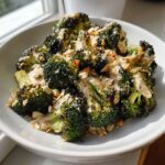 Close-up of a white bowl filled with roasted broccoli salad, drizzled with a creamy dressing and topped with chopped almonds.