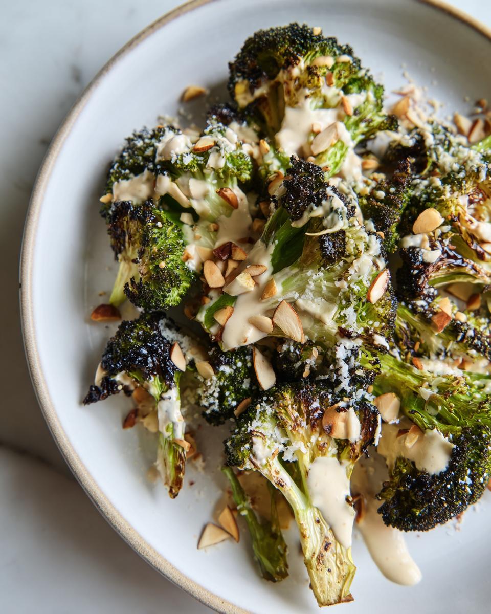 Close-up of roasted broccoli salad florets drizzled with creamy dressing and topped with sliced almonds.