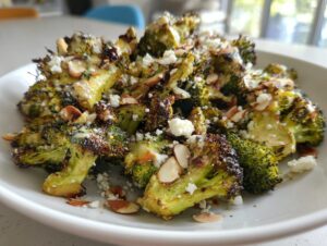 Close-up of perfectly charred roasted broccoli salad topped with crumbled feta cheese and sliced almonds.