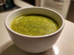 Close-up of a white bowl filled with creamy, bright green roasted broccoli soup, showing fine texture.